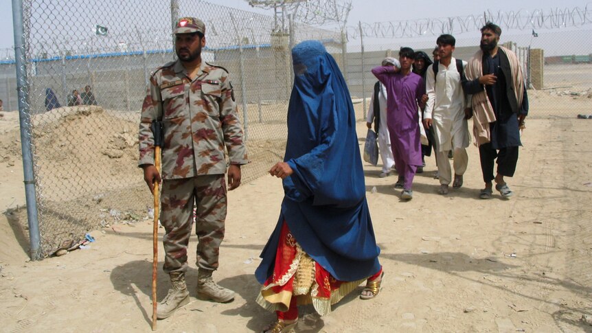 An Afghan woman in a burqa walks past a Pakistani paramilitary soldier along with others at the border checkpoint
