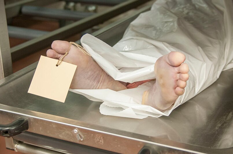 A tagged body lies in a morgue on an aluminium trolley.