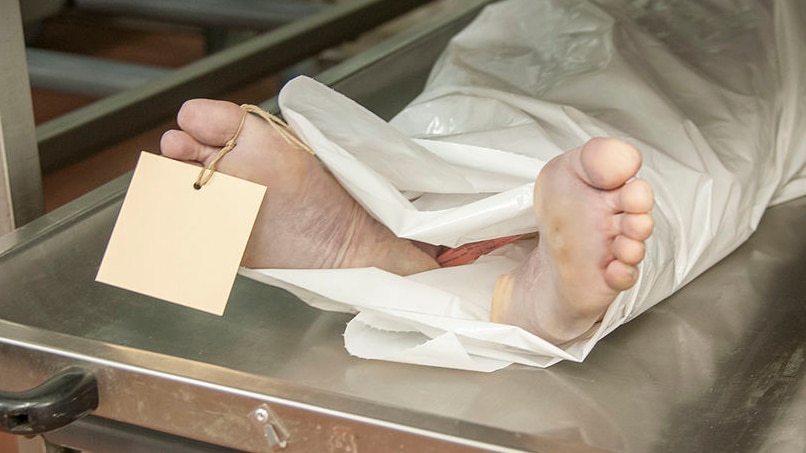 A tagged body lies in a morgue on an aluminium trolley.