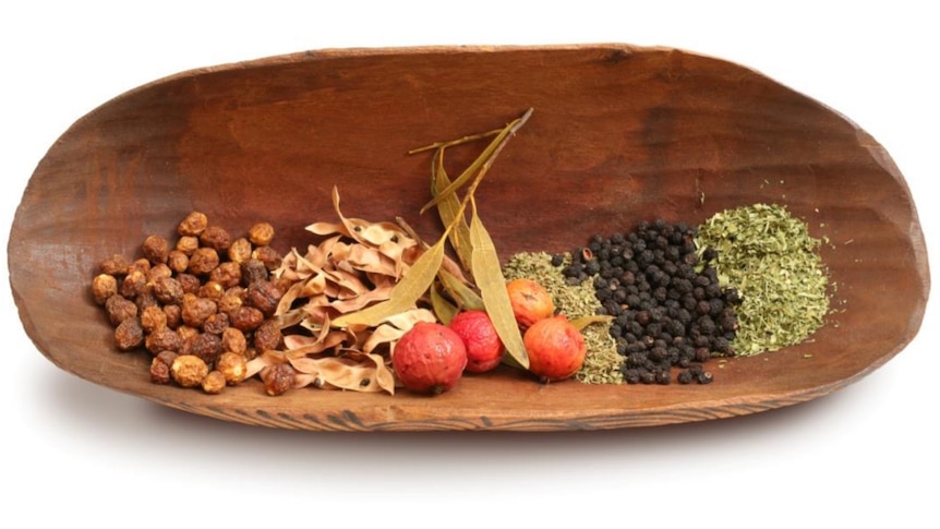A wooden bowl containing a selection of native Australian ingredients including pepper berries, quandongs, and lemon myrtle.