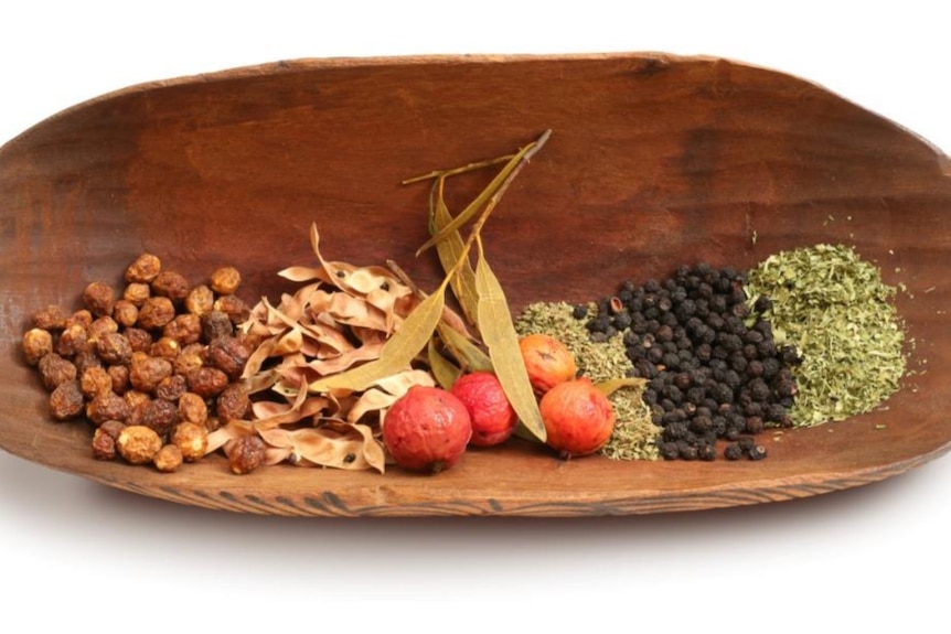 A wooden bowl containing a selection of native Australian ingredients including pepper berries, quandongs, and lemon myrtle.