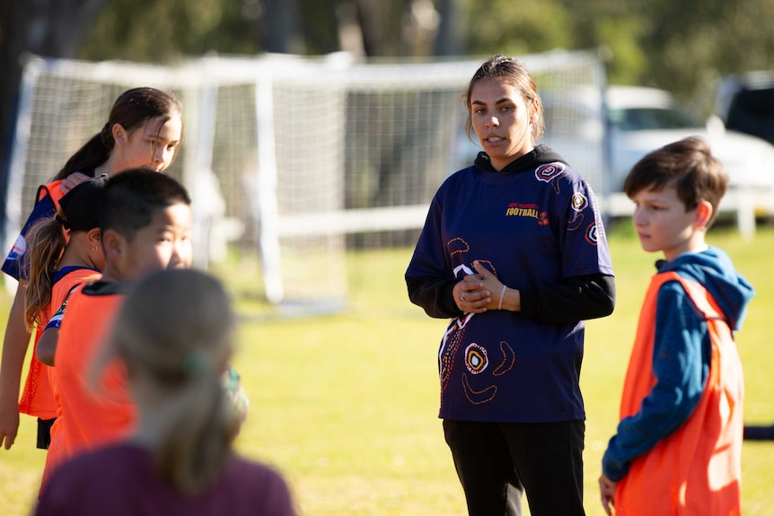 A woman stands among a group of children playing football.