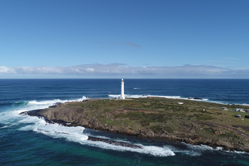 A lighthouse at the edge of a headland overlooking the ocean on a clear day.
