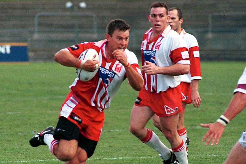 Ian Graham runs with the ball on the football field wearing a red and white jersey.