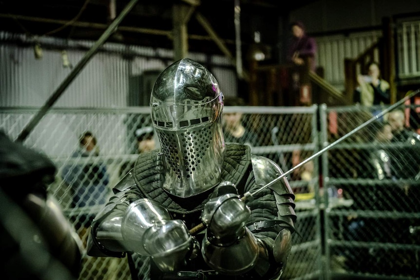 A fighter in armour holds a sword above his head