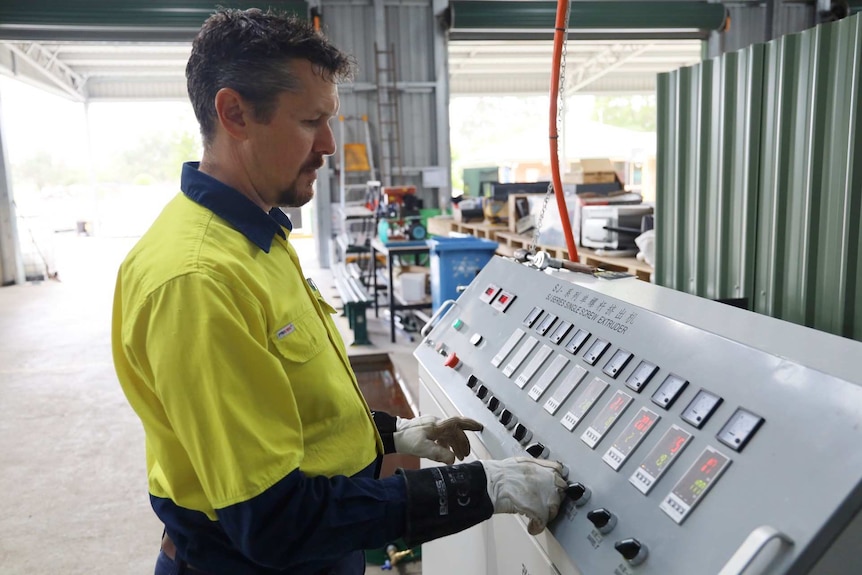 A man in a high vis t-shirt stands next to a machine with buttons reading "extruder"