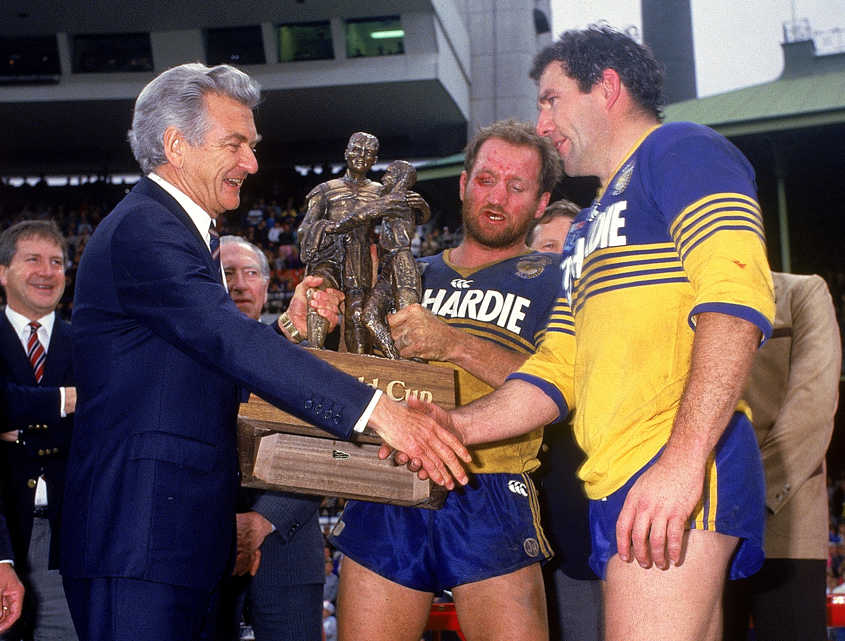 Two rugby league players shake hands with a politician after a grand final
