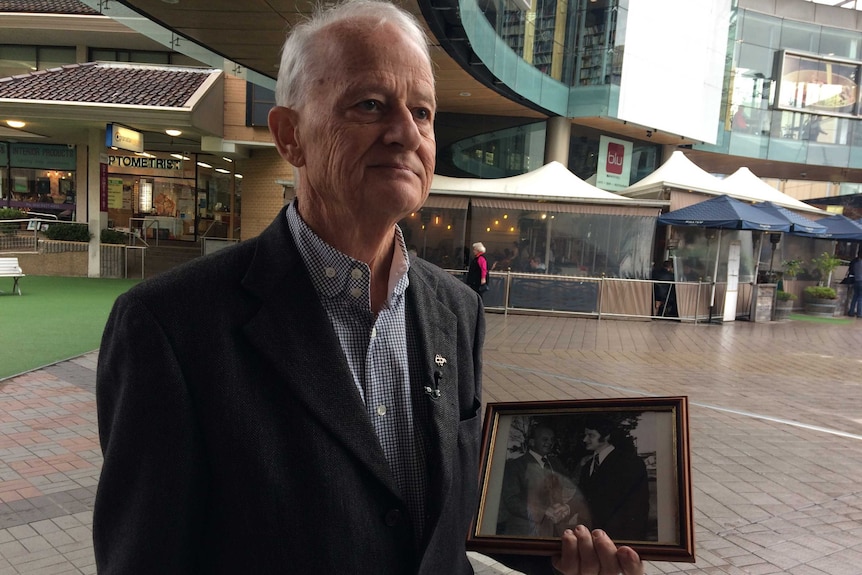 Philip Ruddock stands holding a photo of his father Max.