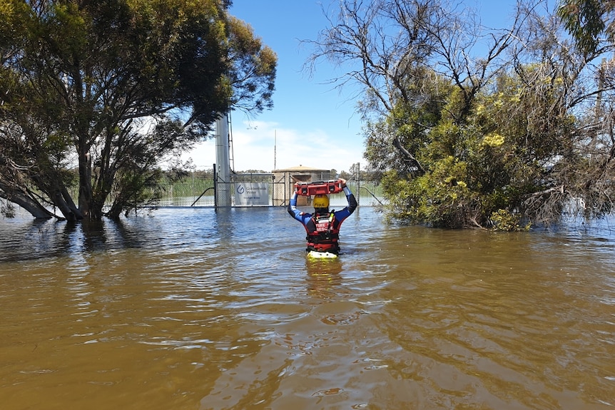 A person in rescue gear wades through muddy water.