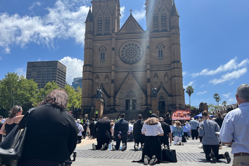Mourners sit in prayer outside a cathedral
