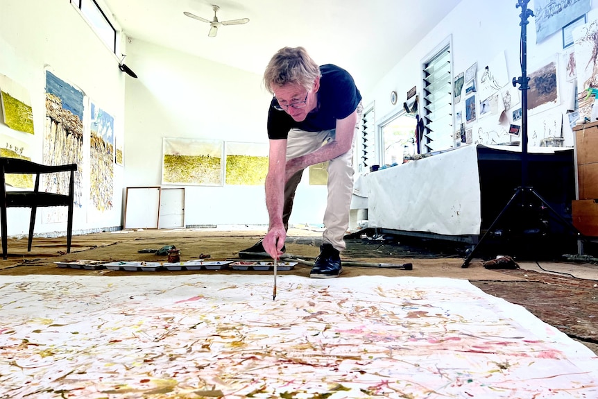 a man with big floor canvas and a paintbrush