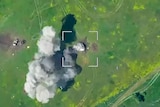 An aerial view of smoke from an explosive attack in a field.