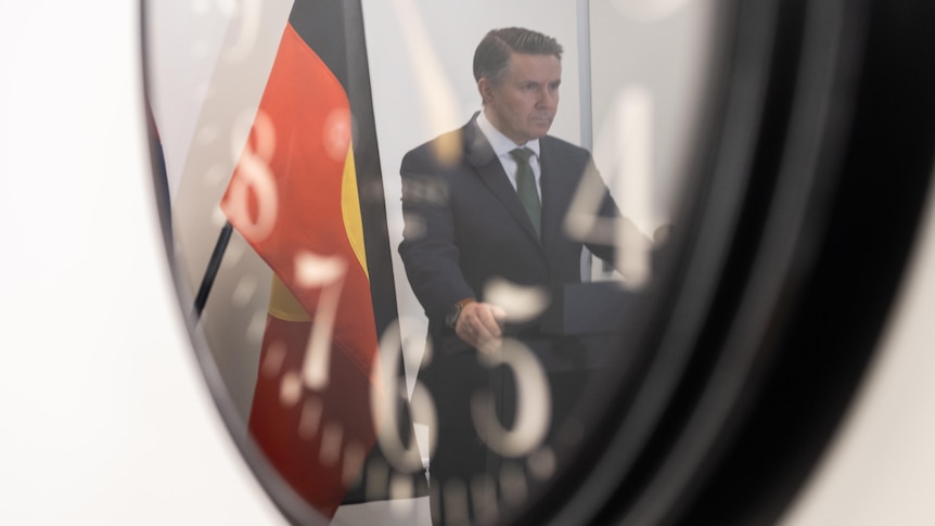 Mark Butler's reflection is seen on a wall clock. 