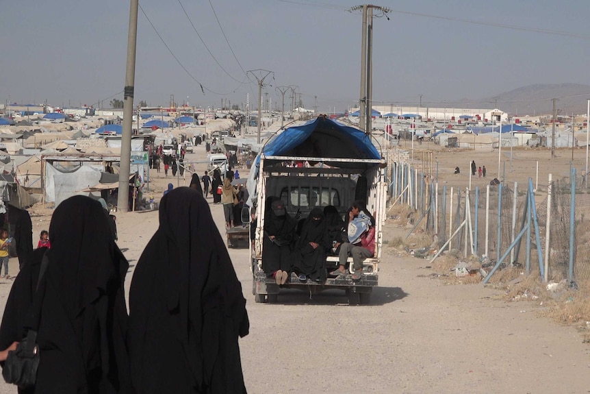 People sit in the back of a truck on a road at a refugee camp in Syria.