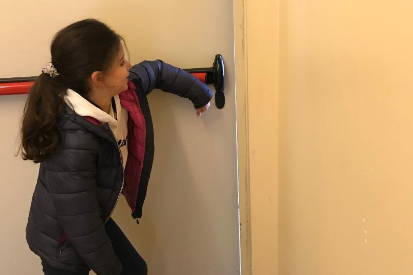 Zoe pushes a door with her elbow.