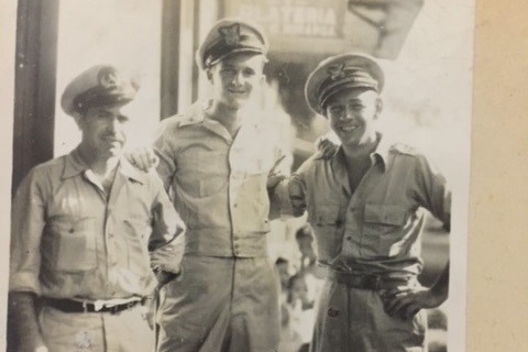 A black and white photo of three men in army fatigues. They are smiling and posing. 