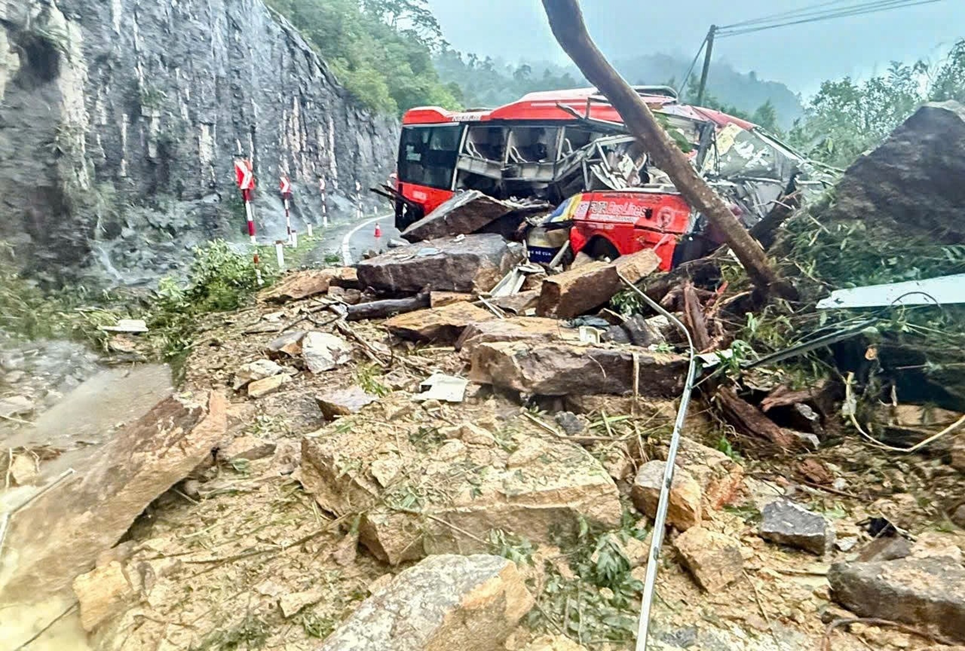 Um ônibus vermelho é encontrado destruído e cercado por pedras e lama em uma estrada montanhosa