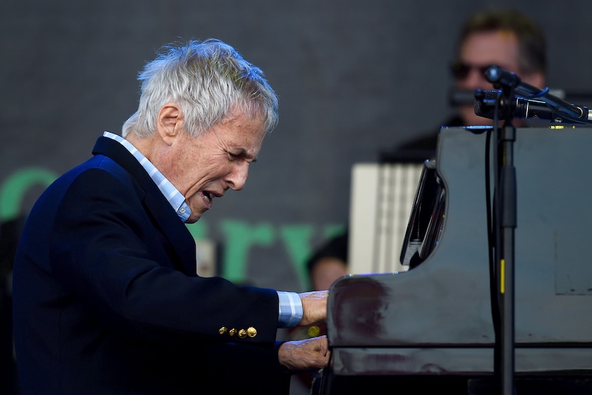 Close up of Burt Bacharach singing while playing the piano on stage.