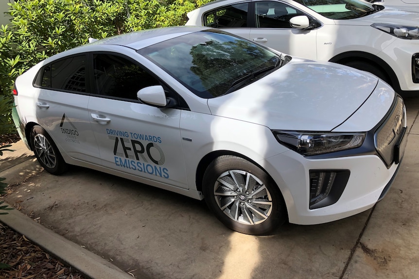 A white sedan car parked in a carpark with Indigo Shire logo and words saying 'Driving towards zero emissions'