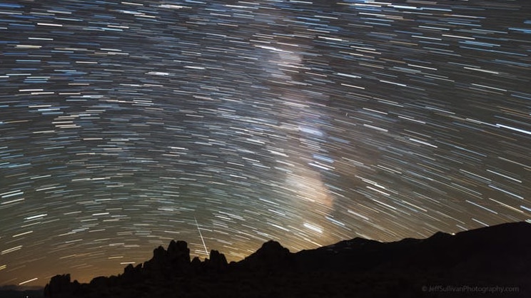 A lone meteor shoots towards the horizon, the opposite direction to thousands of stars in a time lapse photo