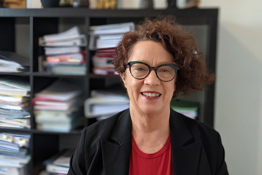 Woman with dark curly hair and glasses with a bookshelf full of folders in the background