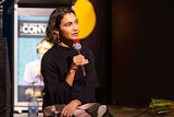 A woman is siting and holding a microphone