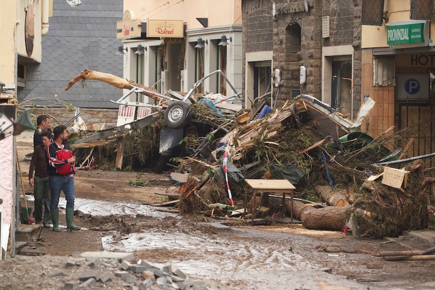 People walk down a street in a Germany town near huge piles of flood debris.