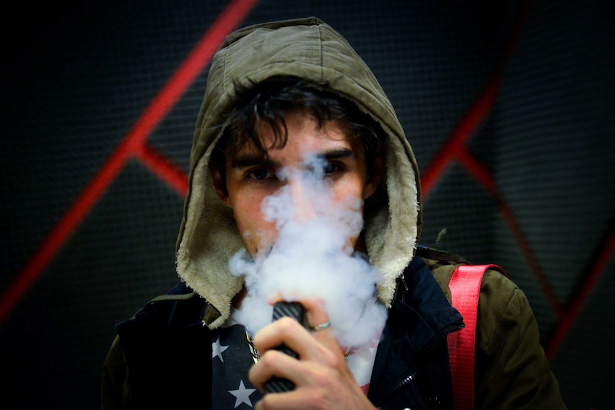 A man in a hoodie vapes
