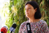 Health Minister Natasha Fyles looks across the camera at a press conference standing in front of microphones.