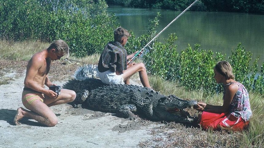 An archival photo of a child fishing as he sits on a crocodile.