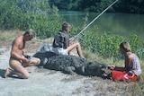 An archival photo of a child fishing as he sits on a crocodile.