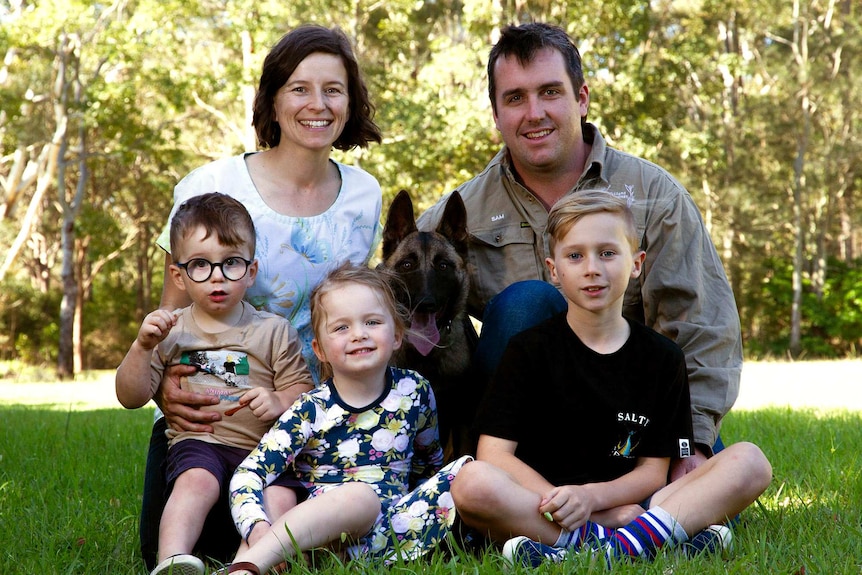 Two aludts, three children and a puppy posing for a family portrait.