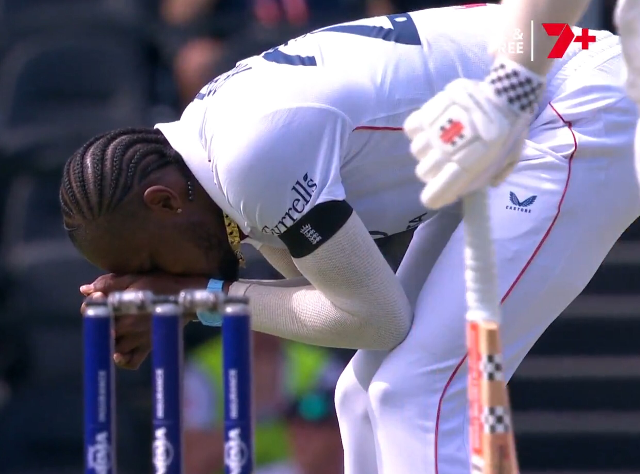 Un jugador de críquet vestido de blanco yace encorvado con las manos en la cabeza. Muñones frente a él, bateador a su derecha.