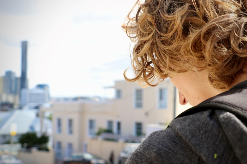 the profile of a curly haired person with the Brisbane city skyline behind