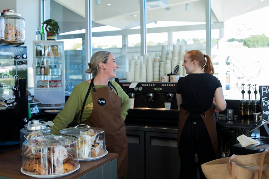 Two women working in a coffee shop look at each other and laugh