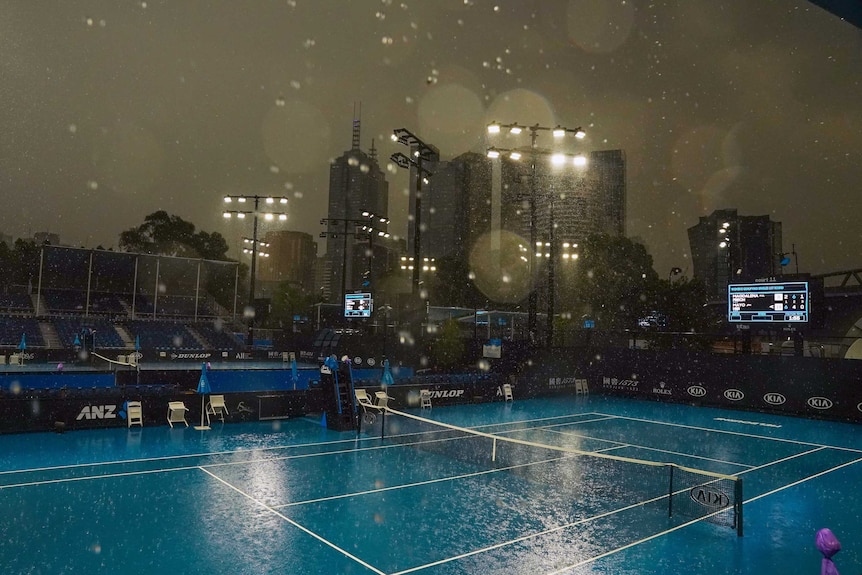 Rain bounces off the court as floodlights shine and the scoreboard glows at the Australian Open.