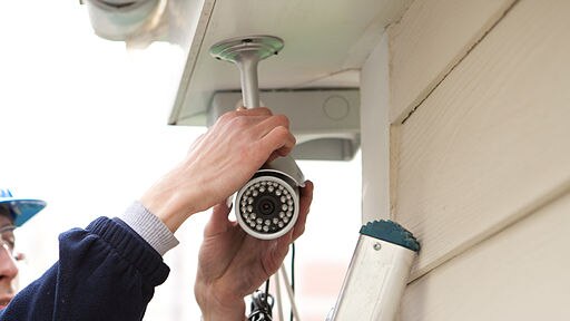 A man installs a security camera outside a home.