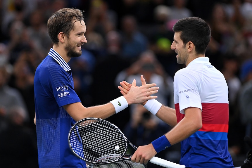 Daniil Medvedev and Novak Djokovic smile and clasp hands