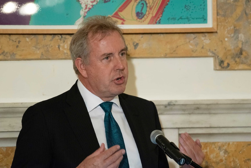 Kim Darroch gesturing in front of a microphone.