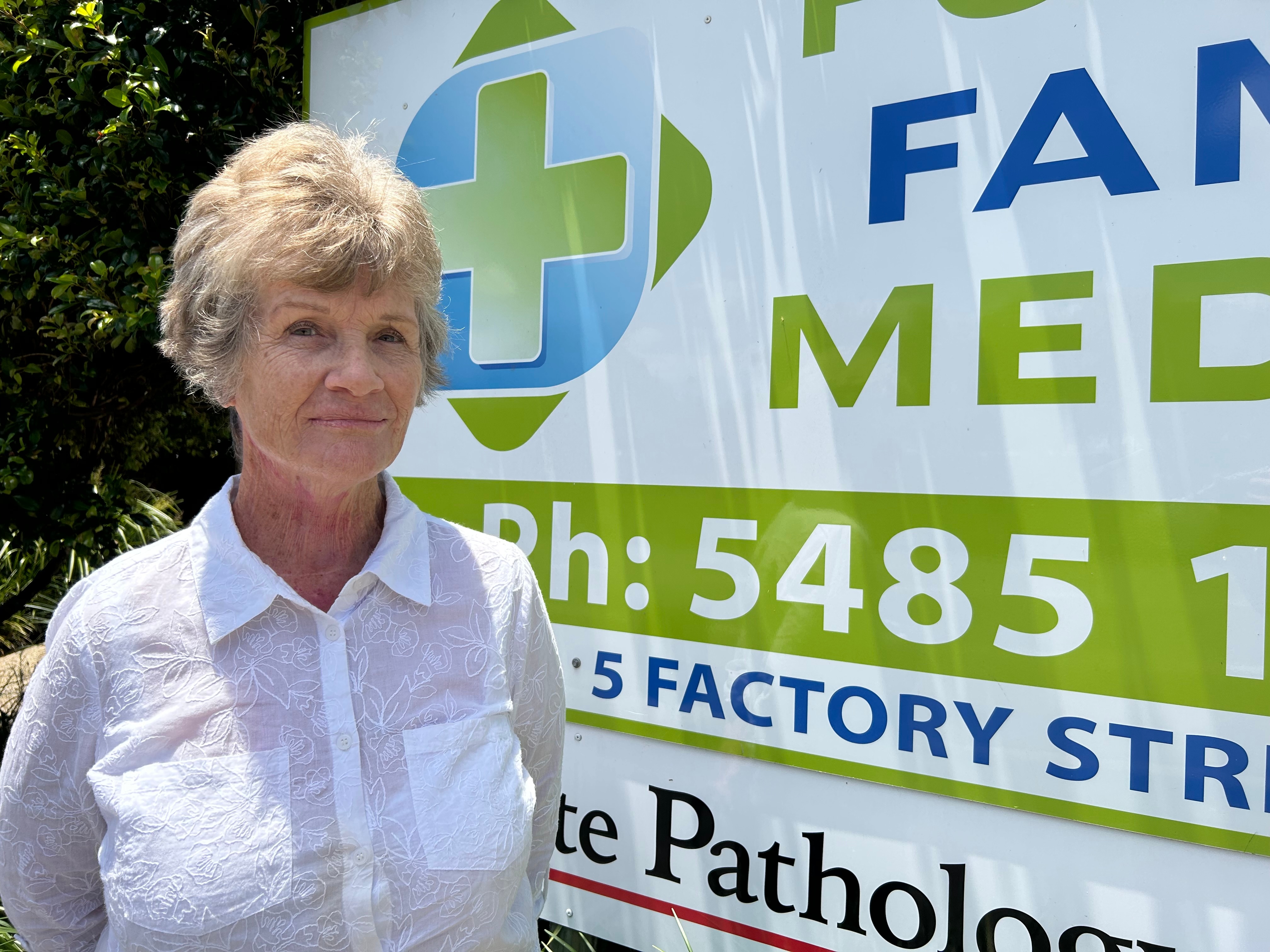 Grey-haired woman standing in front of GP sign