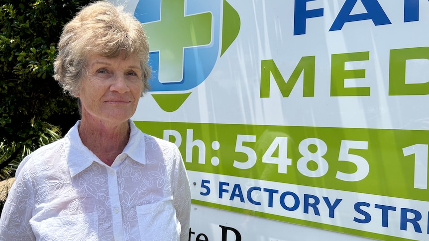 Grey-haired woman standing in front of GP sign