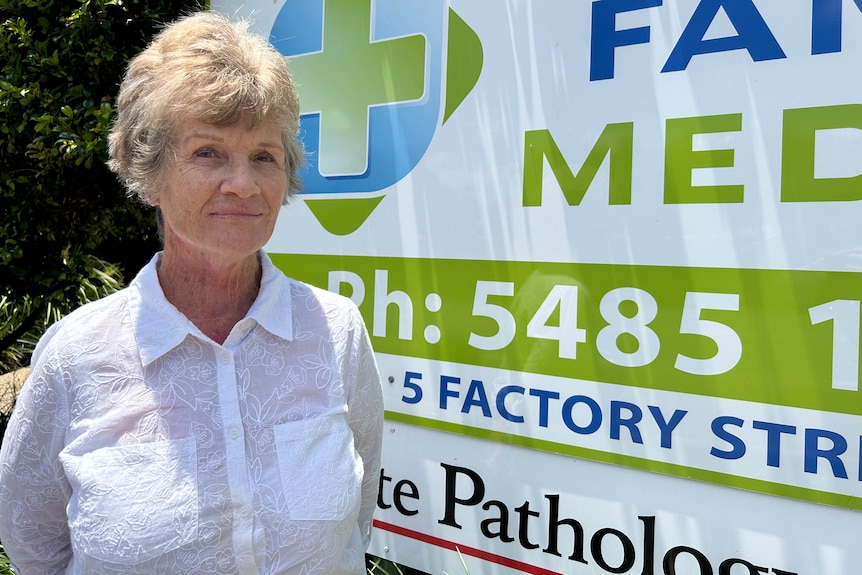 Grey-haired woman standing in front of GP sign