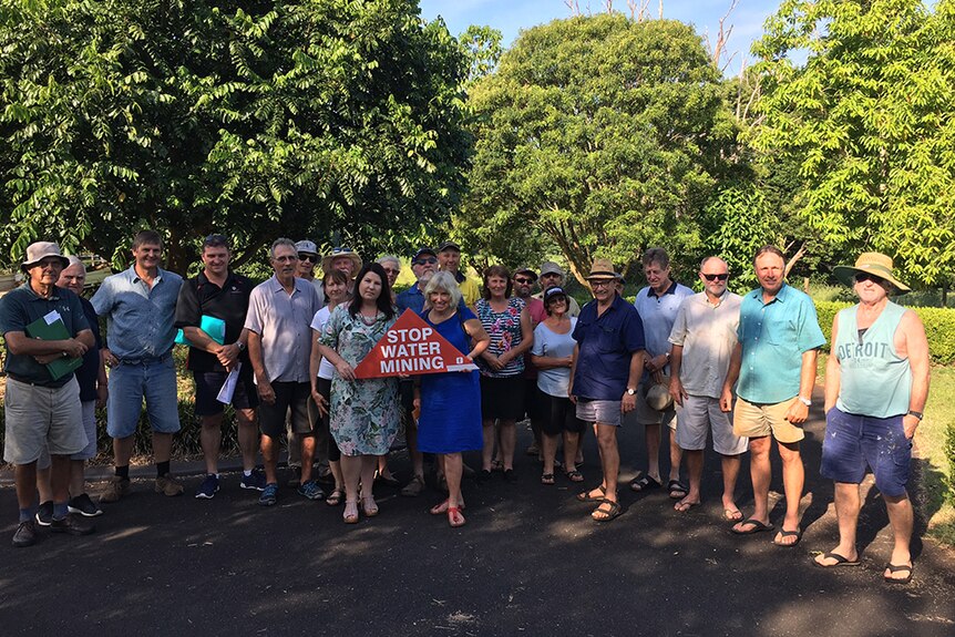 A group of 20 farmers with a red Stop Water Mining sign.