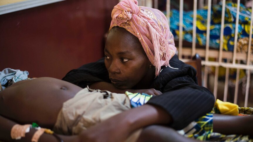 A woman sits beside her son suffering from malaria