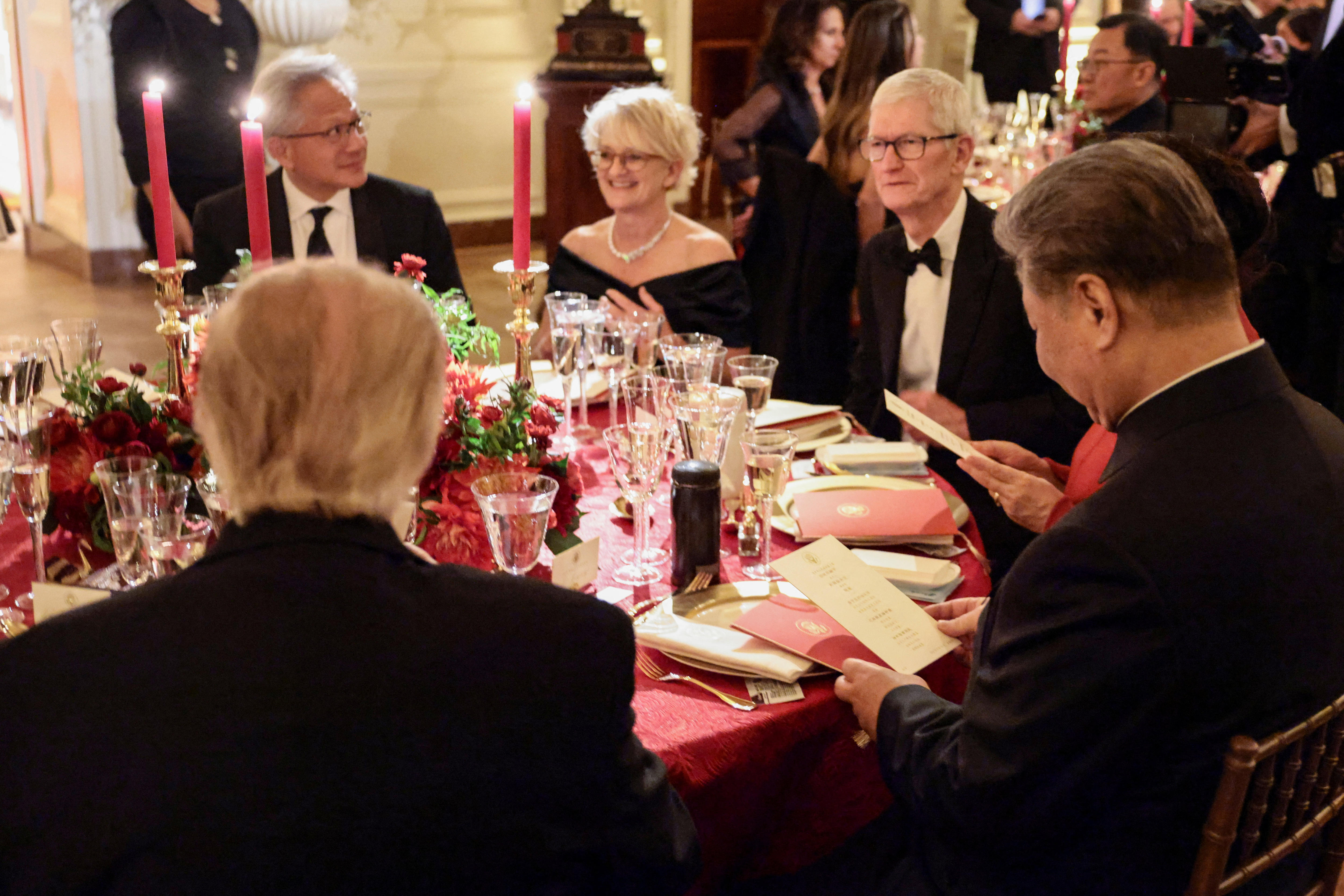 Four men including Huang and a woman dine at an elaborate table with orchids, red candles and tablecloths.