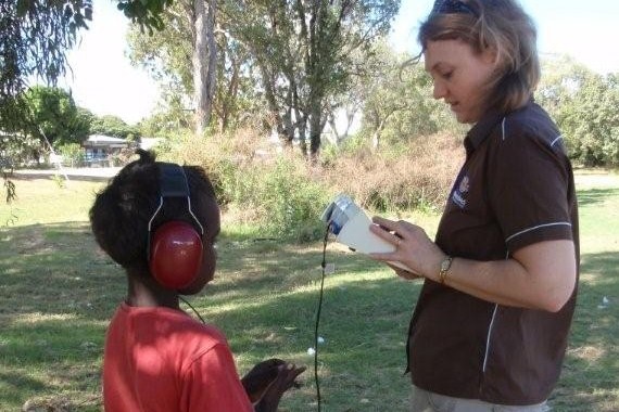 Audiologist standing opposite young indigenous boy performing hearing check
