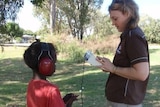 Audiologist standing opposite young indigenous boy performing hearing check