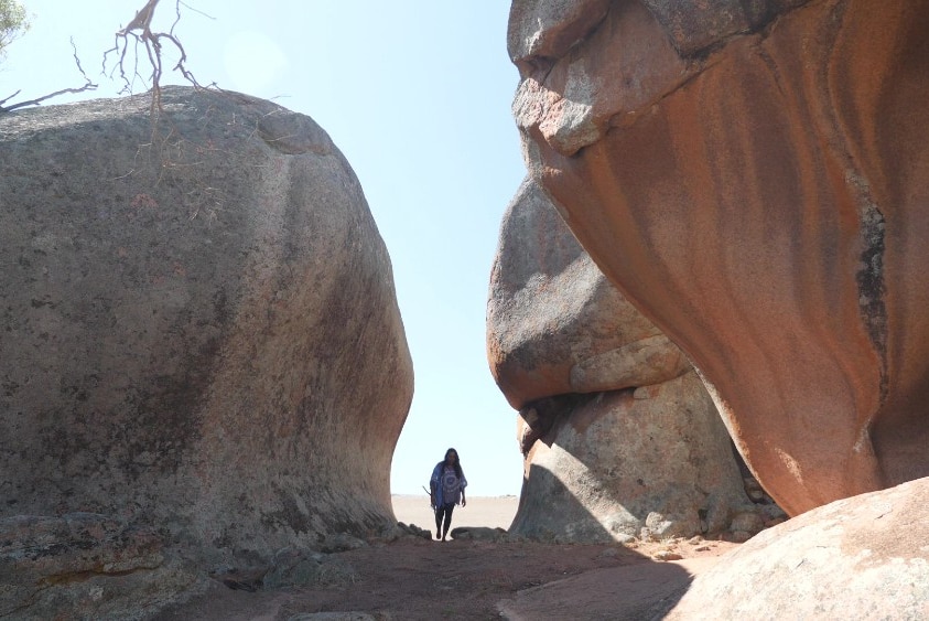 A woman walks among towering cliff faces.