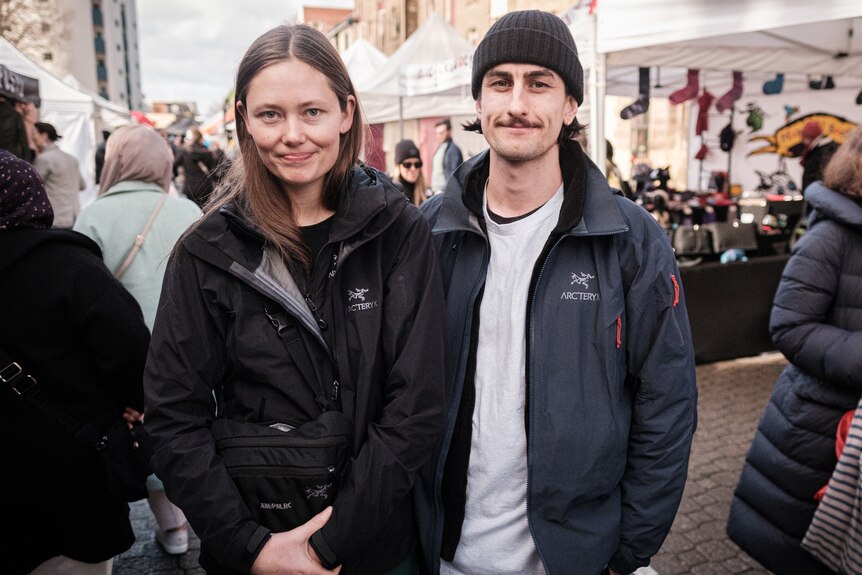 A young woman and a man in a beanie stand in a market