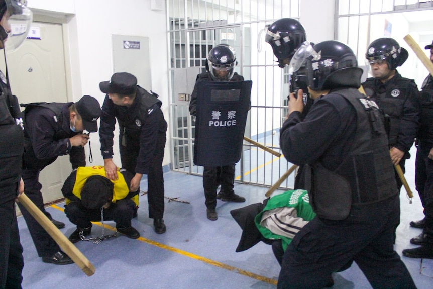 A group of police in riot gear in what looks like a cell.